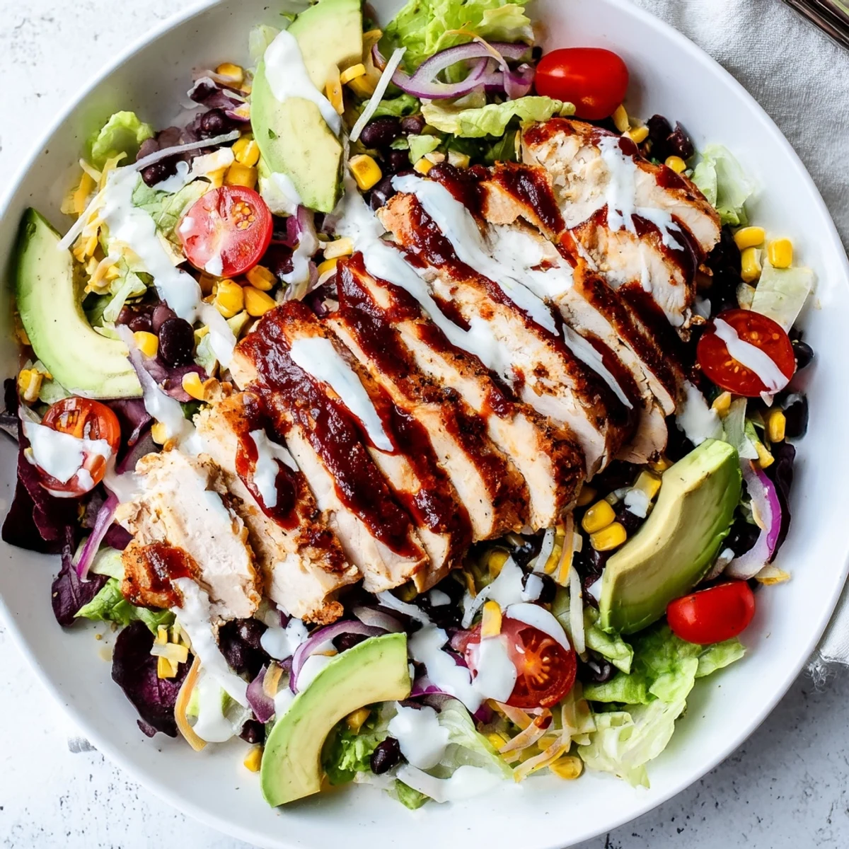 Juicy, smoky BBQ chicken slices rest on crisp romaine lettuce, alongside charred corn, black beans, and cherry tomatoes for a vibrant meal.  