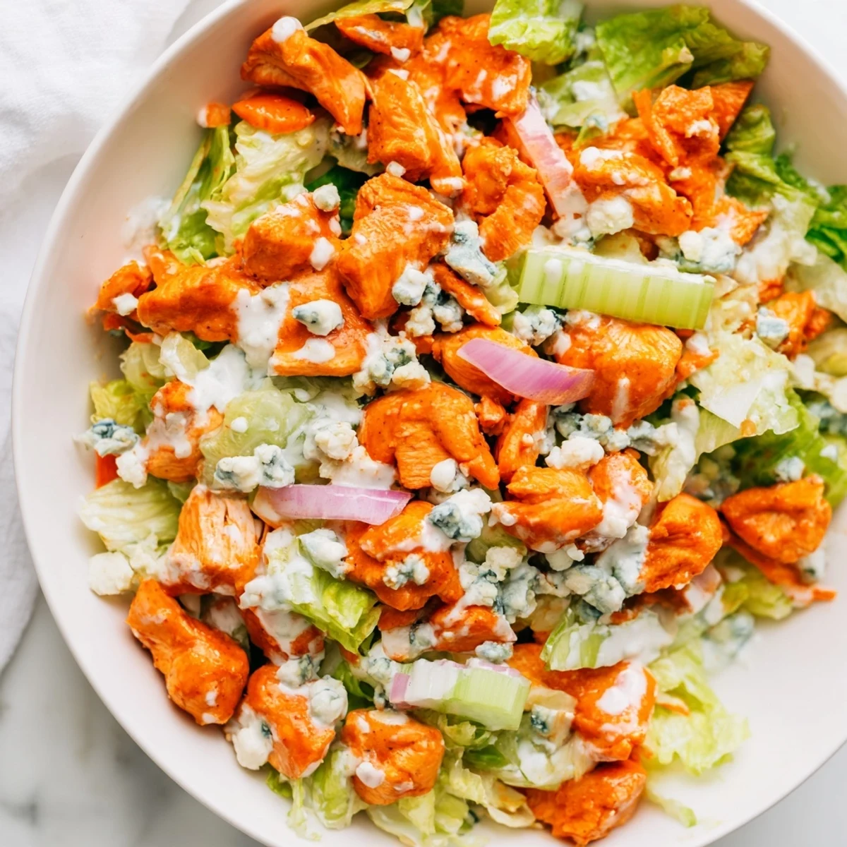 Freshly chopped romaine and spicy Buffalo chicken pieces topped with crumbled blue cheese in a rustic salad bowl.