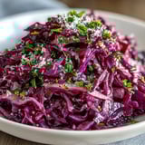 A close view of Red Cabbage Coleslaw With Apple and Parmesan, with shaved Parmesan and bright parsley garnish on a platter.