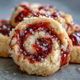 Close-up of Raspberry Swirl Shortbread Cookies highlighting the jam swirls and crumbly texture on a rustic wooden table.