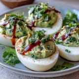 Vibrant deviled eggs with avocado filling and zesty lime, finished with a bold Sriracha kick for heat lovers.  