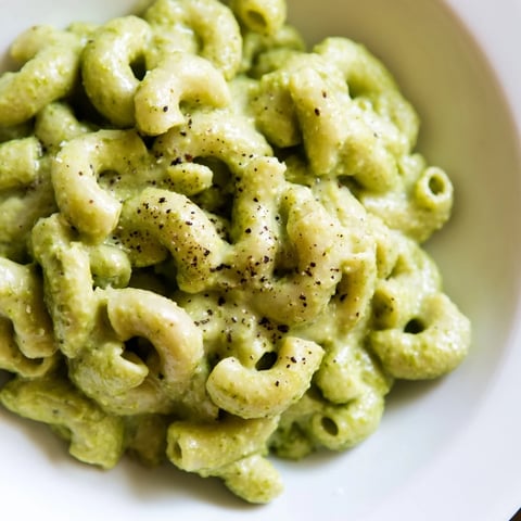 Creamy Avocado Pesto Mac served warm in a white bowl, garnished with fresh basil and grated Parmesan cheese.