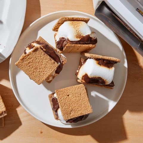 Four golden-brown s'mores made in the air fryer, with gooey marshmallow and melted chocolate peeking out.