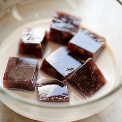 A close-up view of creamy Coffee Jelly Dessert in a clear glass, featuring rich brown jelly squares and fluffy white sweetened cream.