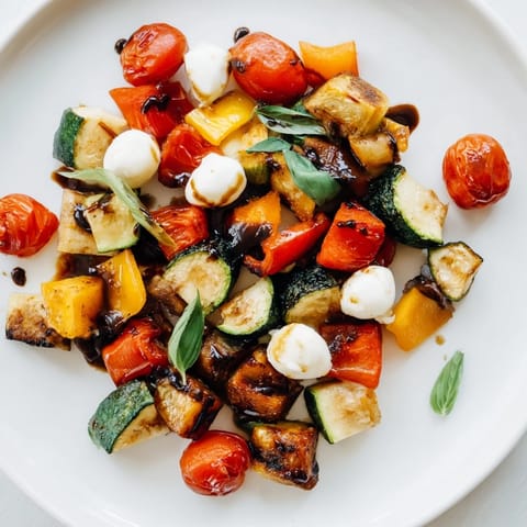 A close-up view shows fresh torn basil leaves and a glossy balsamic drizzle over the colorful, caramelized vegetables and mozzarella.