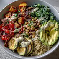 Vibrant Black-Eyed Pea Buddha Bowl with roasted sweet potatoes, red peppers, and creamy tahini dressing, garnished with fresh avocado slices and herbs.